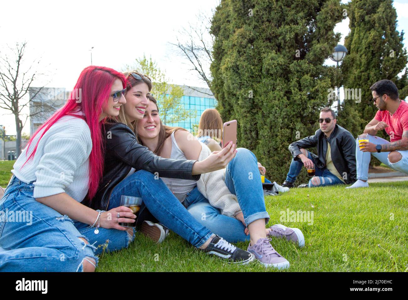 group of three friends having their photo taken with the telephone while sitting on the grass having a drink Stock Photo