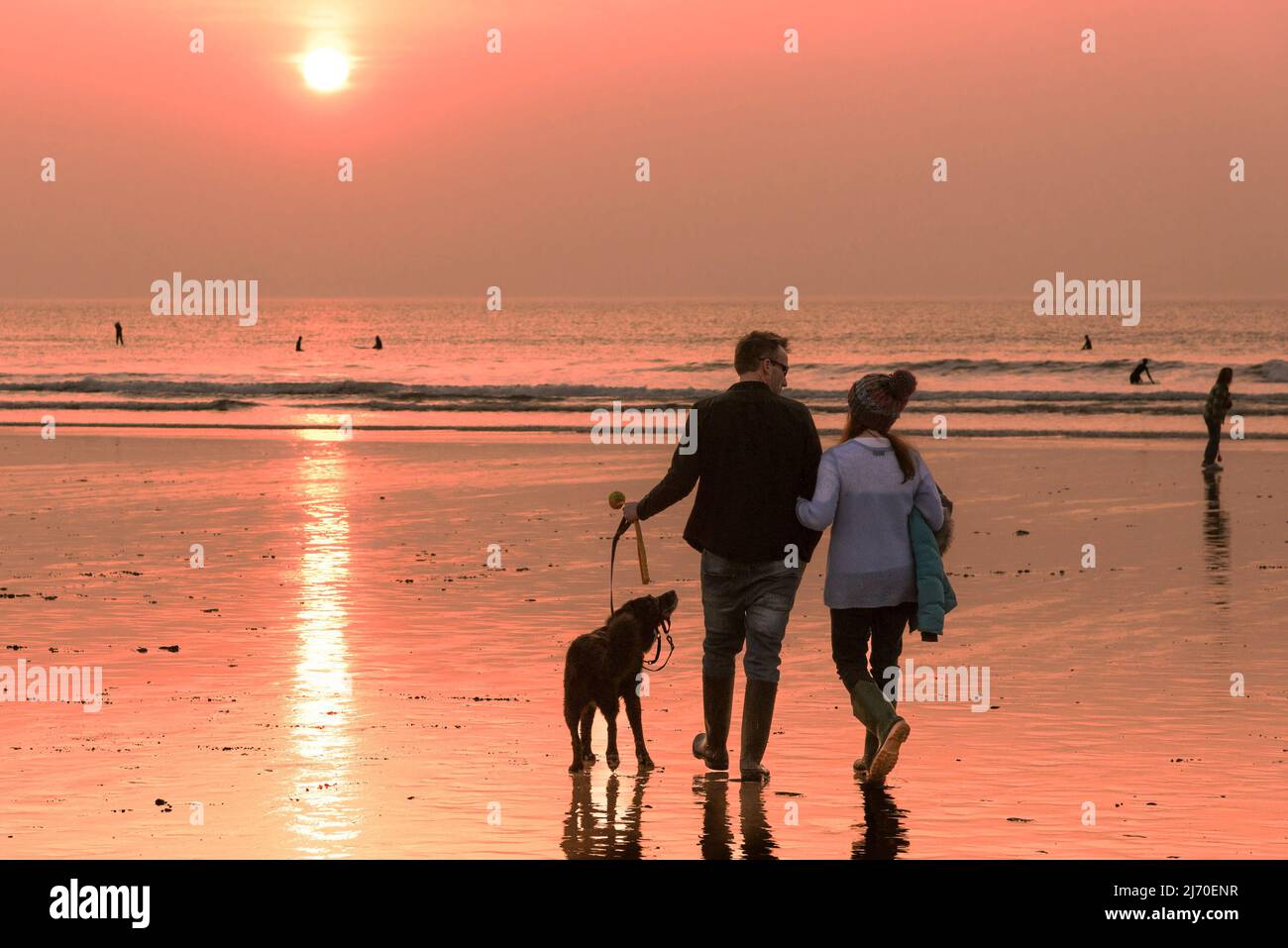 Dog walkers walking on Fistral Beach during an intense sunset in Newquay in Cornwall in the UK. Stock Photo