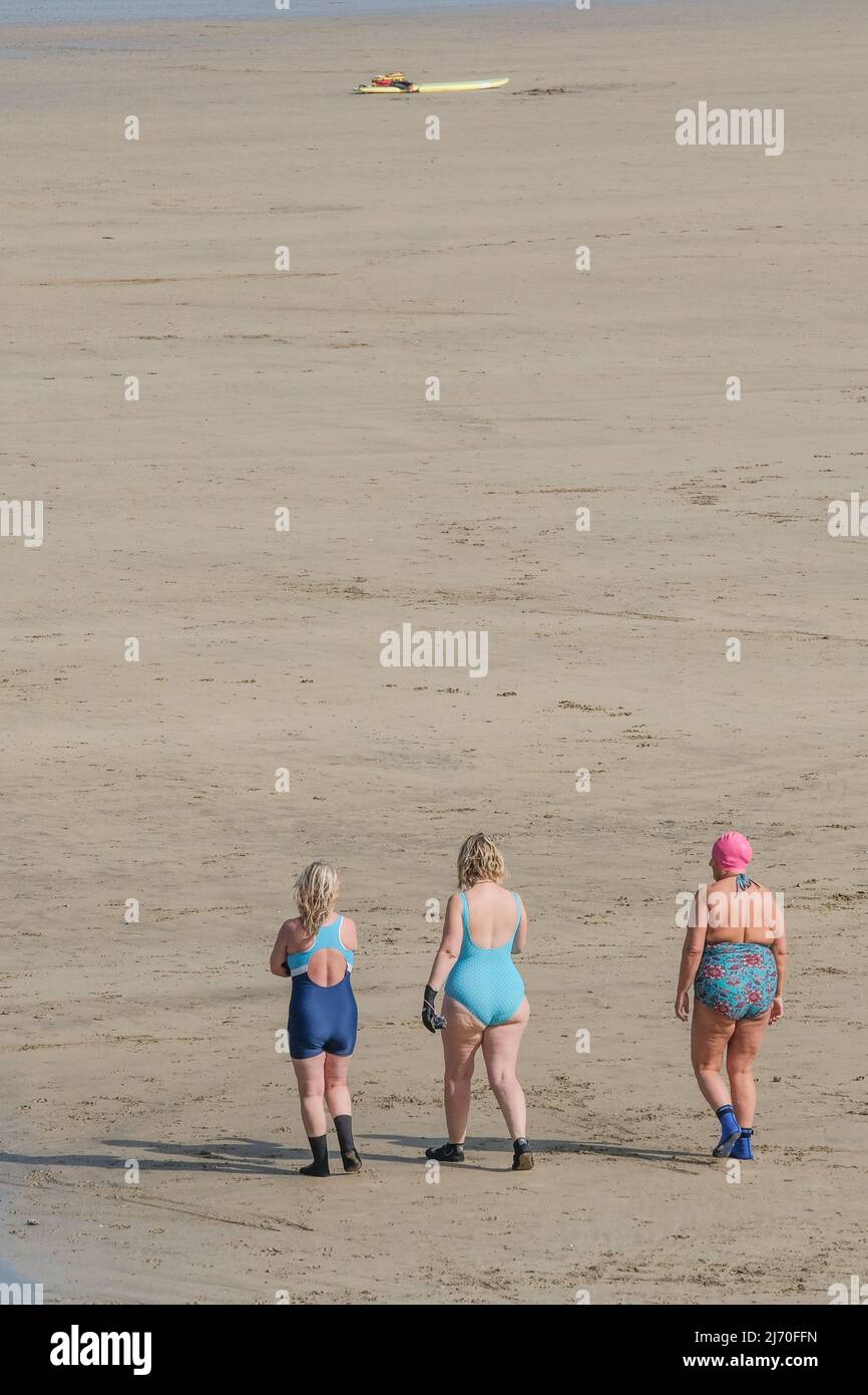 Three mature women walking on Towan Beach to the sea in Newquay in Cornwall in the UK. Stock Photo