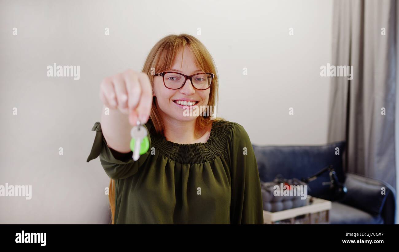 Young red-haired woman showing keys to her new apartment and looking at ...