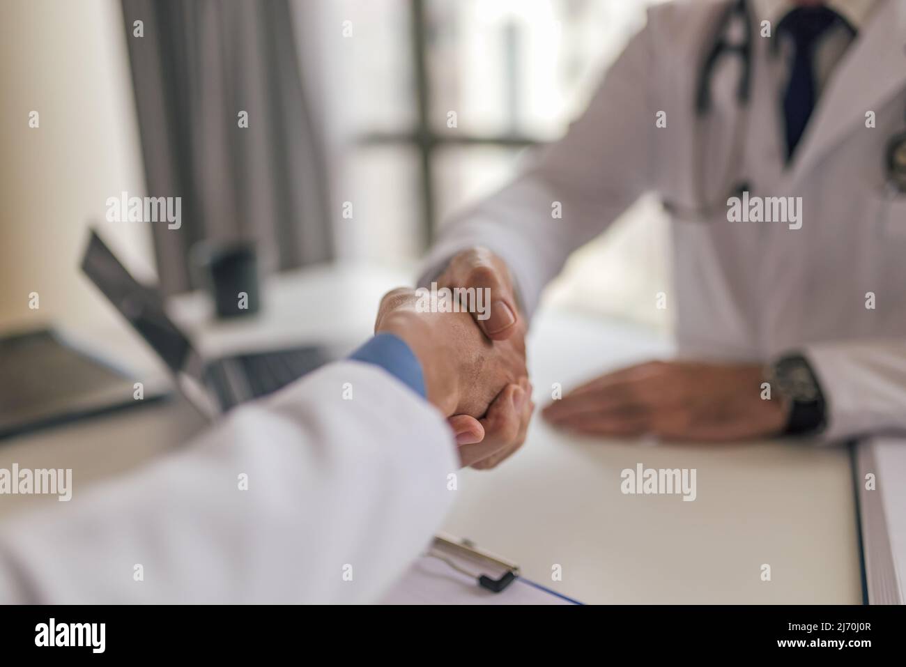 Midsection of female doctor shaking hands with patient, Healthcare worker greeting man while sitting at desk, they are meeting in clinic. Focus on the Stock Photo