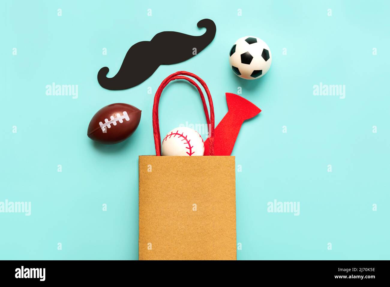 Happy Father's Day. Top view of shopping bag with false mustache,false bow tie and sports balls with space for text over blue background. Father's Day Stock Photo