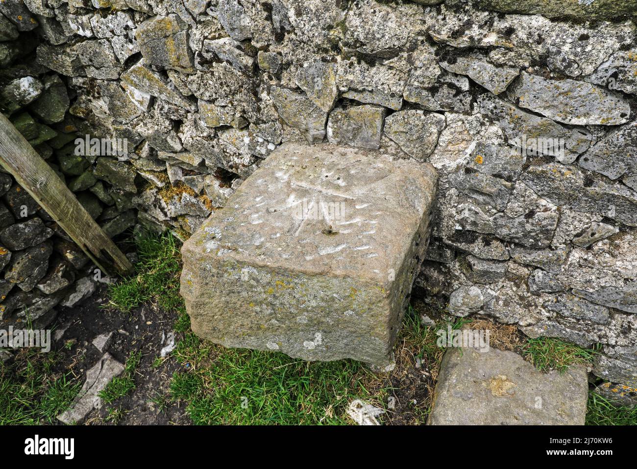 An Ordnance Survey bench mark scratched on a limestone stone stile in a dry stone wall, Derbyshire, England, UK Stock Photo