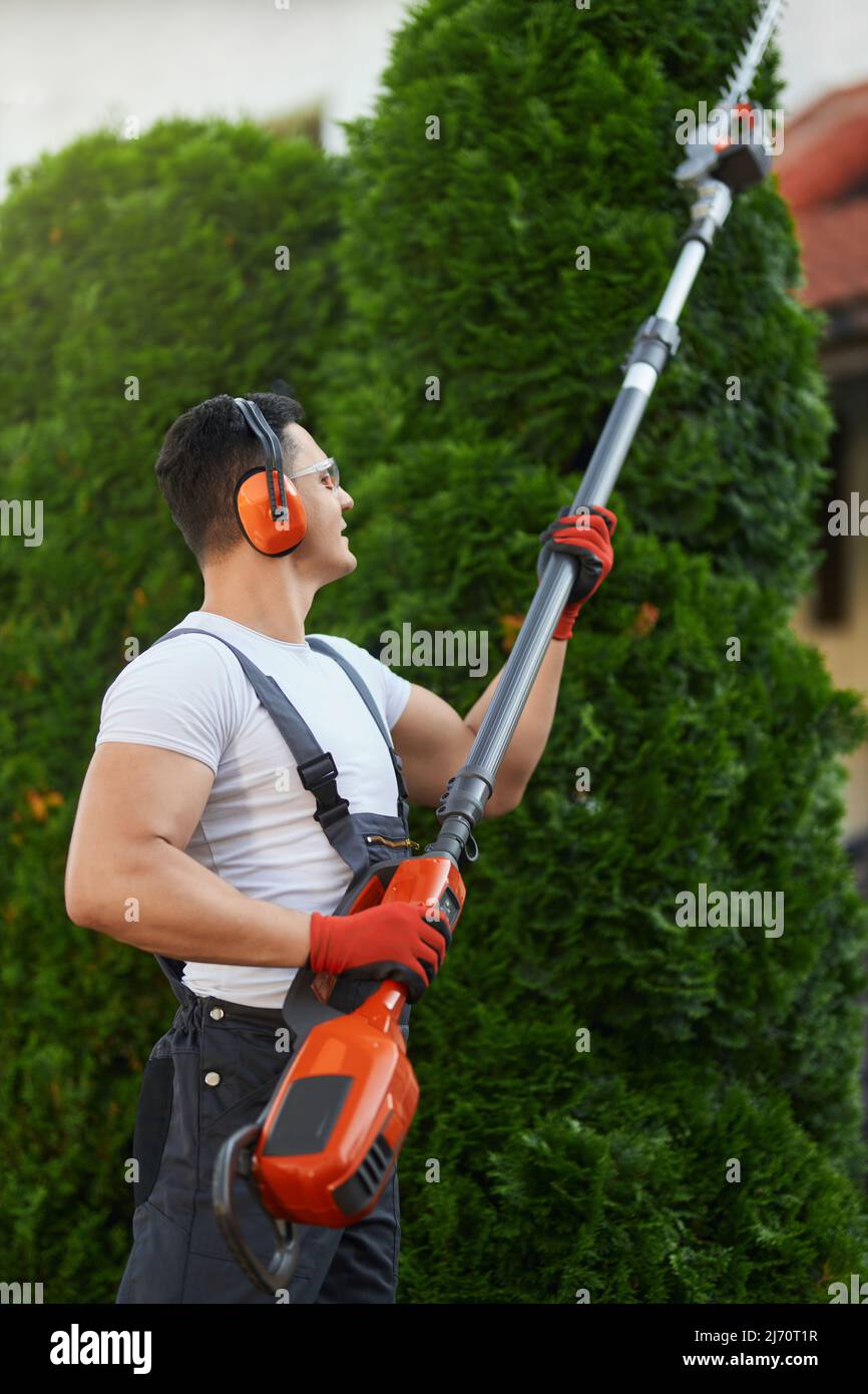 Caucasian handyman in overalls, protective glasses, and gloves pruning