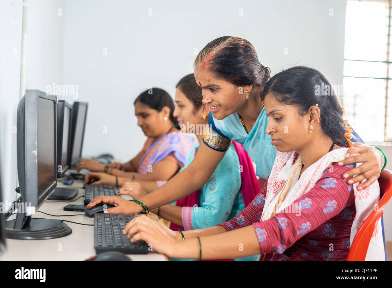 Teacher helping or teaching students during computer class training - concept of learning, personal support and technology. Stock Photo