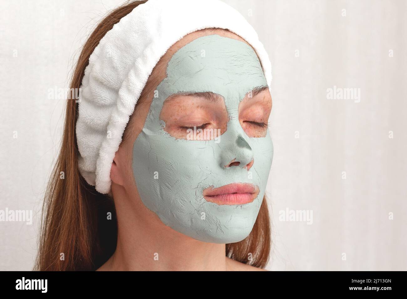 Woman with white band on head with blue dry clay mask on face with closed eyes over white background Stock Photo