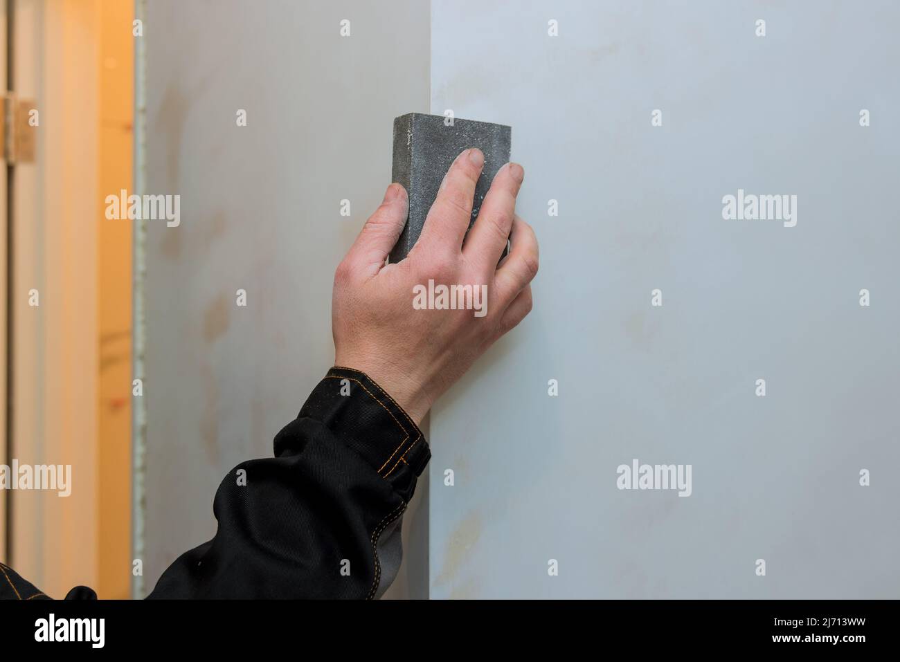 Worker sanding the drywall mud using sand trowel during renovation the