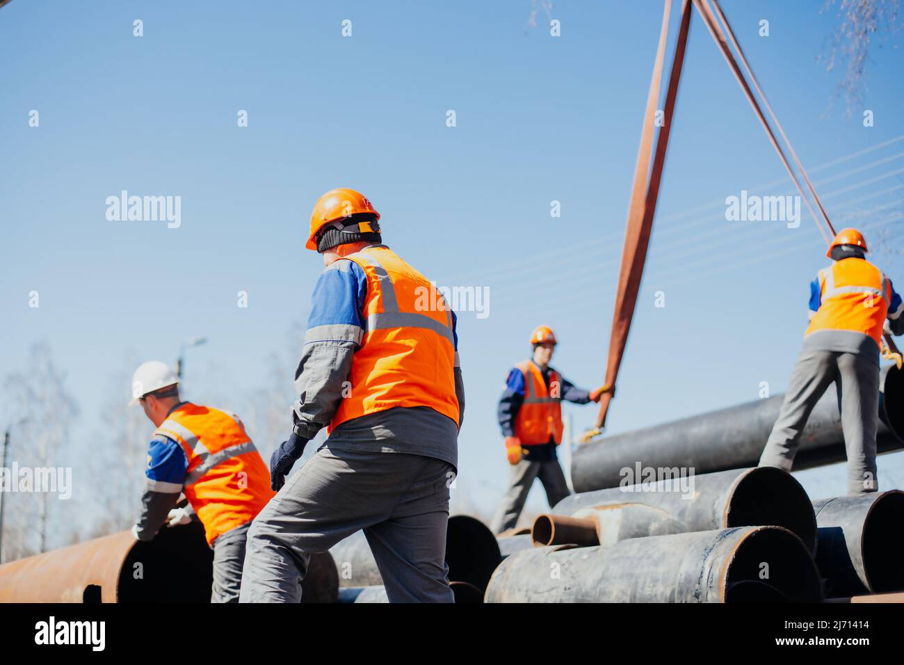 Group of slingers in construction helmets and vests on street unload metal pipes. Real scene. Workflow Stock Photo