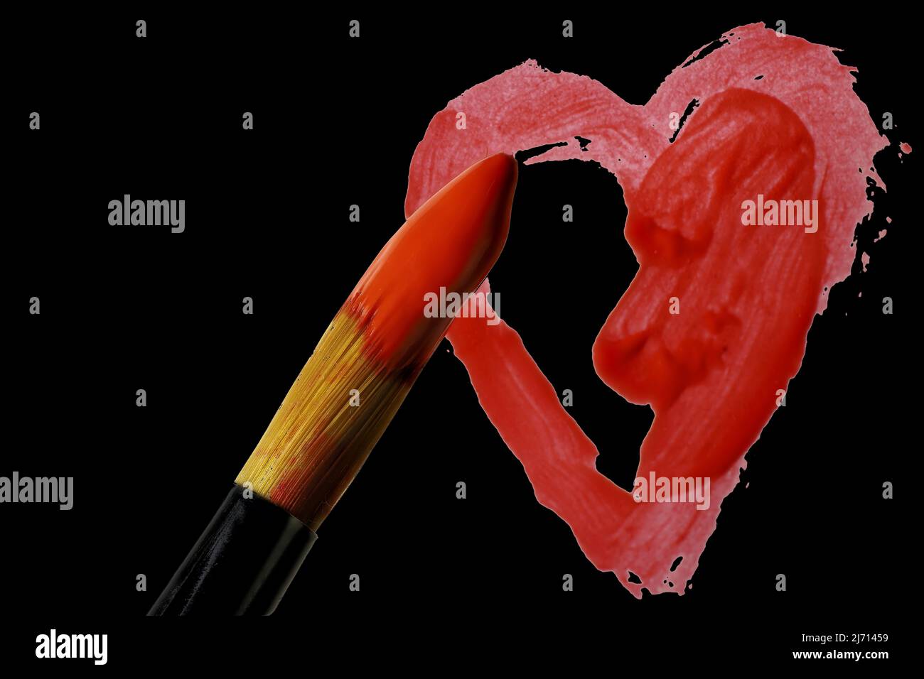 Tip of artist's brush dipped in red acrylic over partially completed painted heart on black background Stock Photo