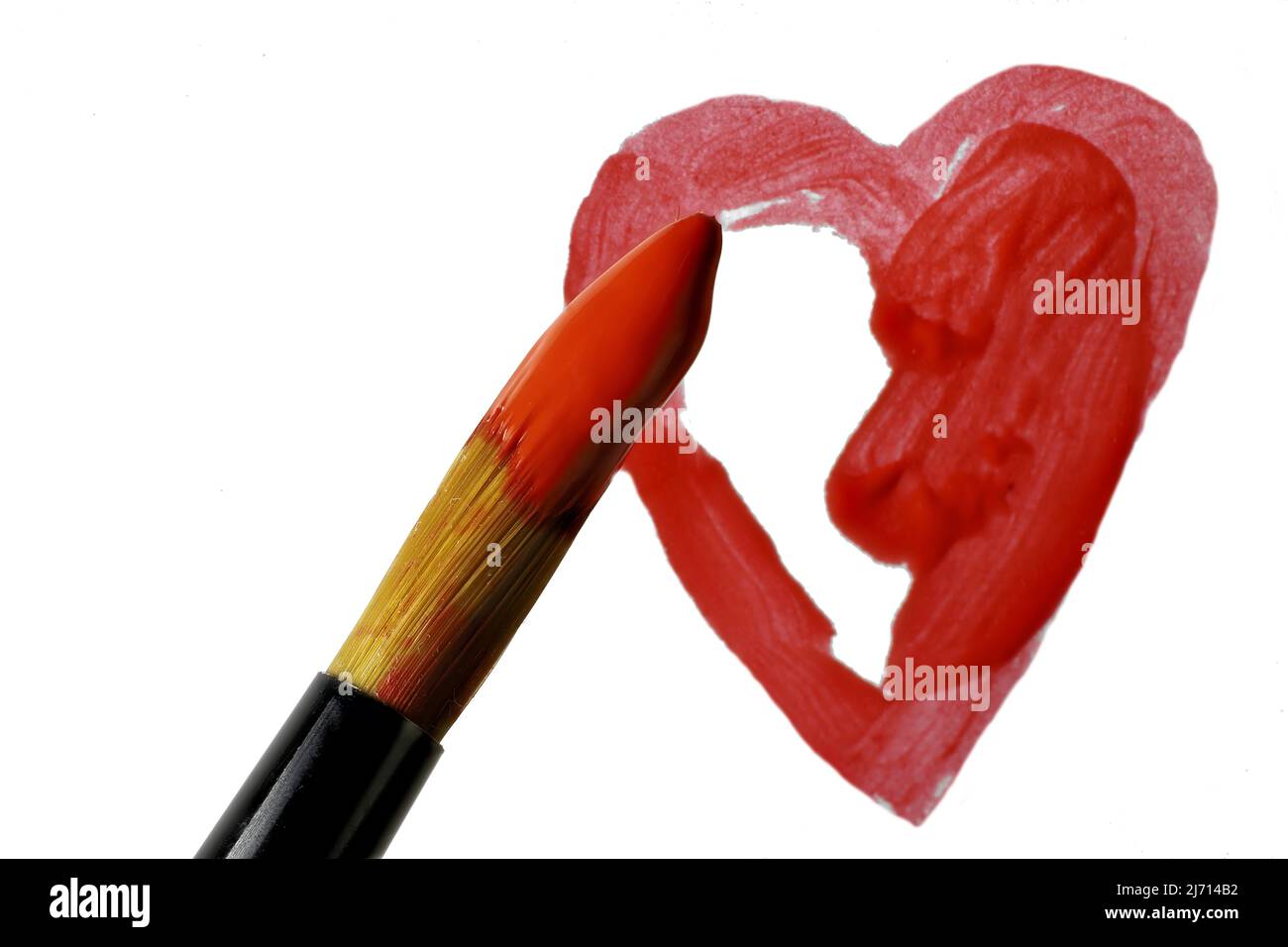 Tip of artist's brush dipped in red acrylic over partially completed painted heart on white background Stock Photo