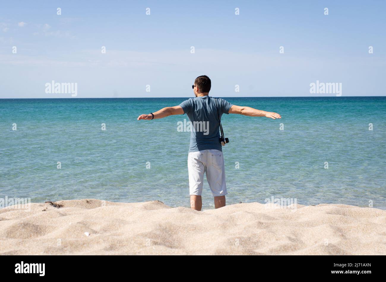 Man stands by the sea and enjoys it. The concept of oneness with nature and relaxation, tourism. Front view. Stock Photo