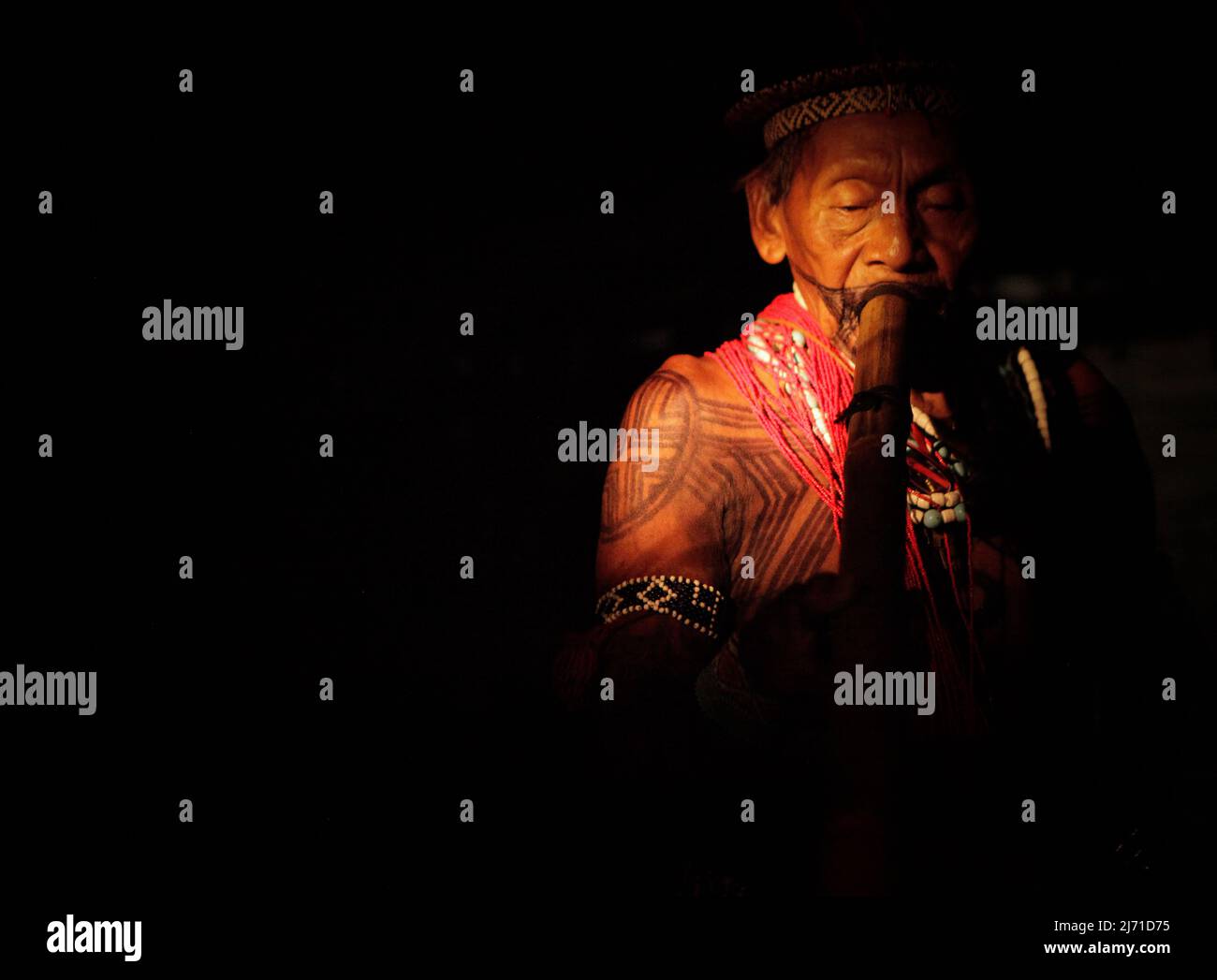 Leader of the Asurini Indigenous tribe in the Brazilian Amazon playing music instrument in the darkness . Xingu  River, Brazil, 2010. Stock Photo