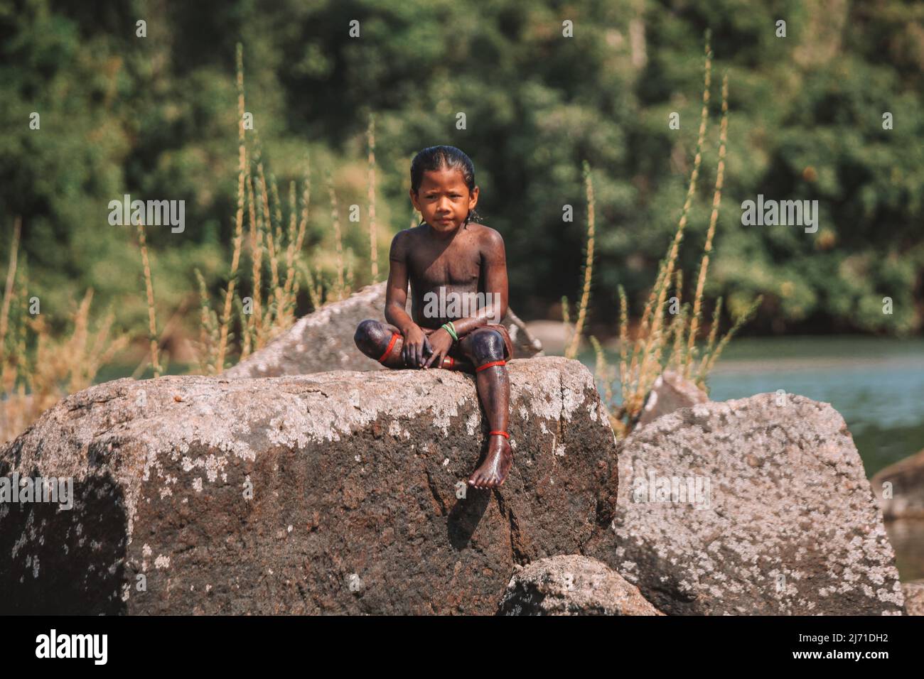 Indian boy from tribe in the Amazon, sitiing on a rock by the Xingu River in Brazil, 2010. Stock Photo