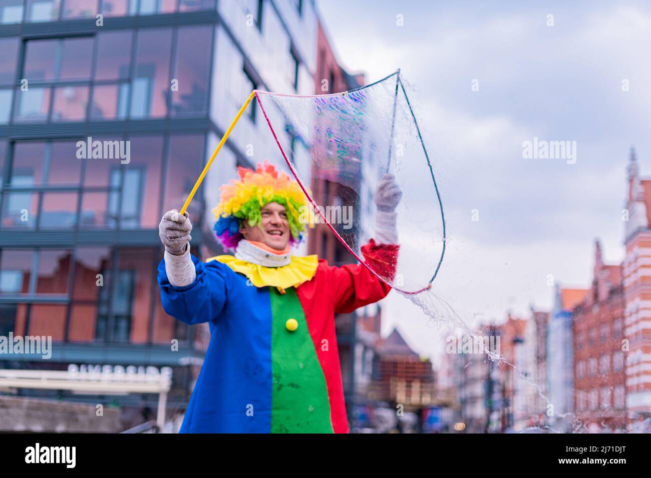 Gdansk,PL-16 Mar 22: Clown creating huge and bright soap bubbles in the air. Colorful clown providing entertainment for passing through people on the Stock Photo