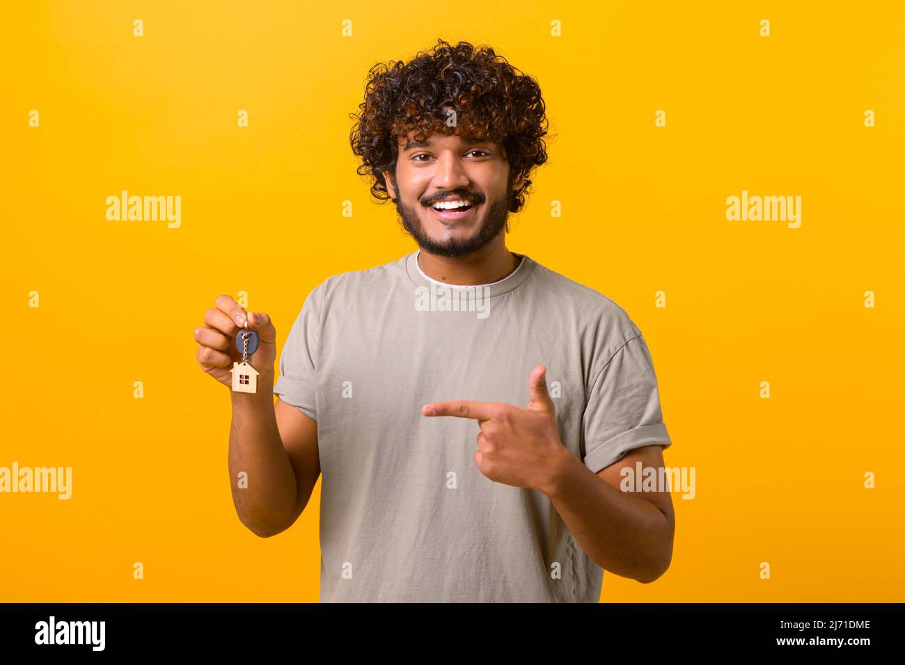 Happy young Indian guy showing keys and points finger on it standing isolated on yellow, happy multiracial hispanic man with keys Stock Photo