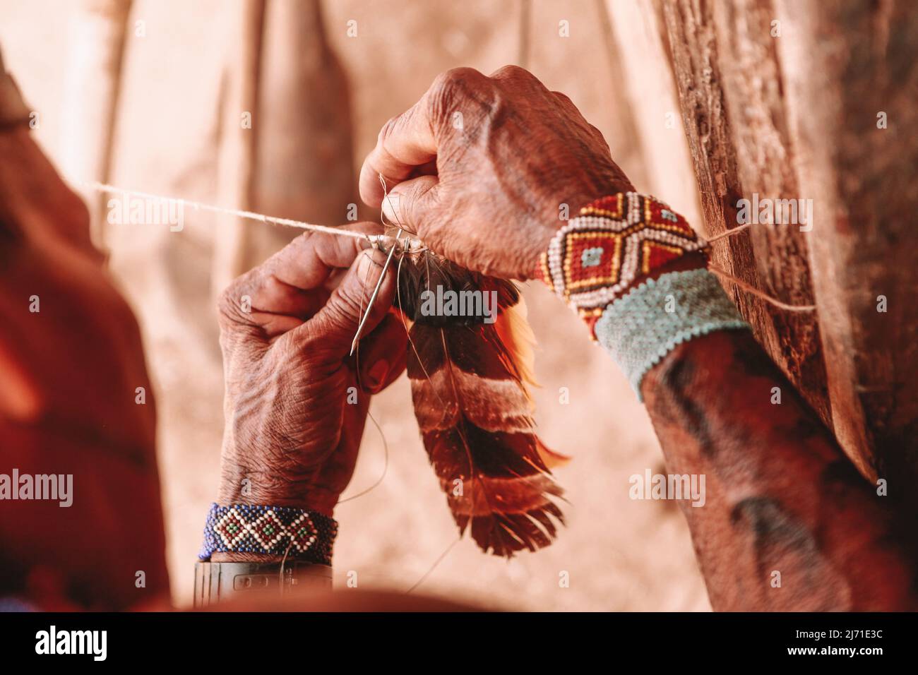 Indian man crafting a cocar headdress made of feathers. Rio Xingu ...