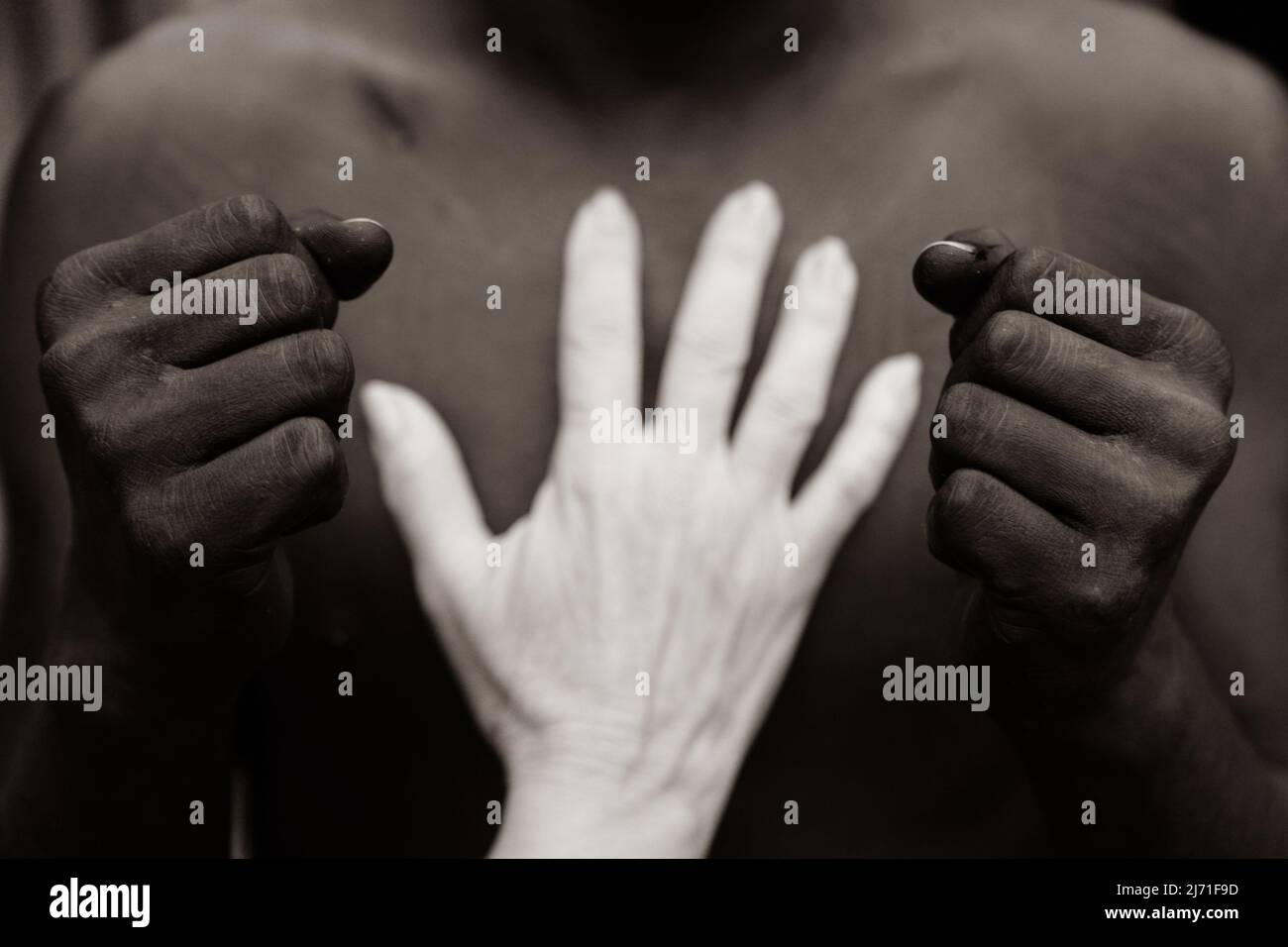 Black person's fist and white person's hand touching his chest Stock Photo