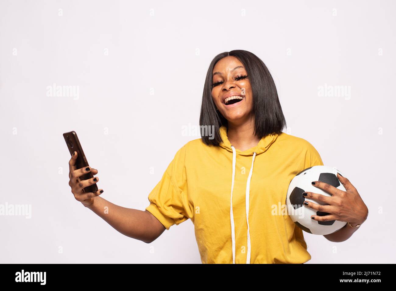 happy black lady holding a football and using her phone Stock Photo