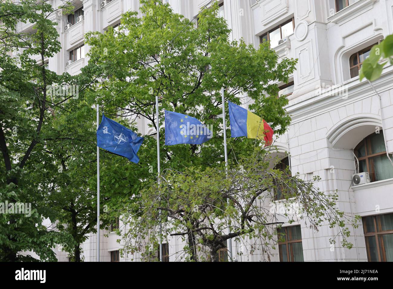 Three flags of Romania, European Union and NATO next to each other in Bucharest, Romania, conceptually illustrating the present geopolitical situation Stock Photo
