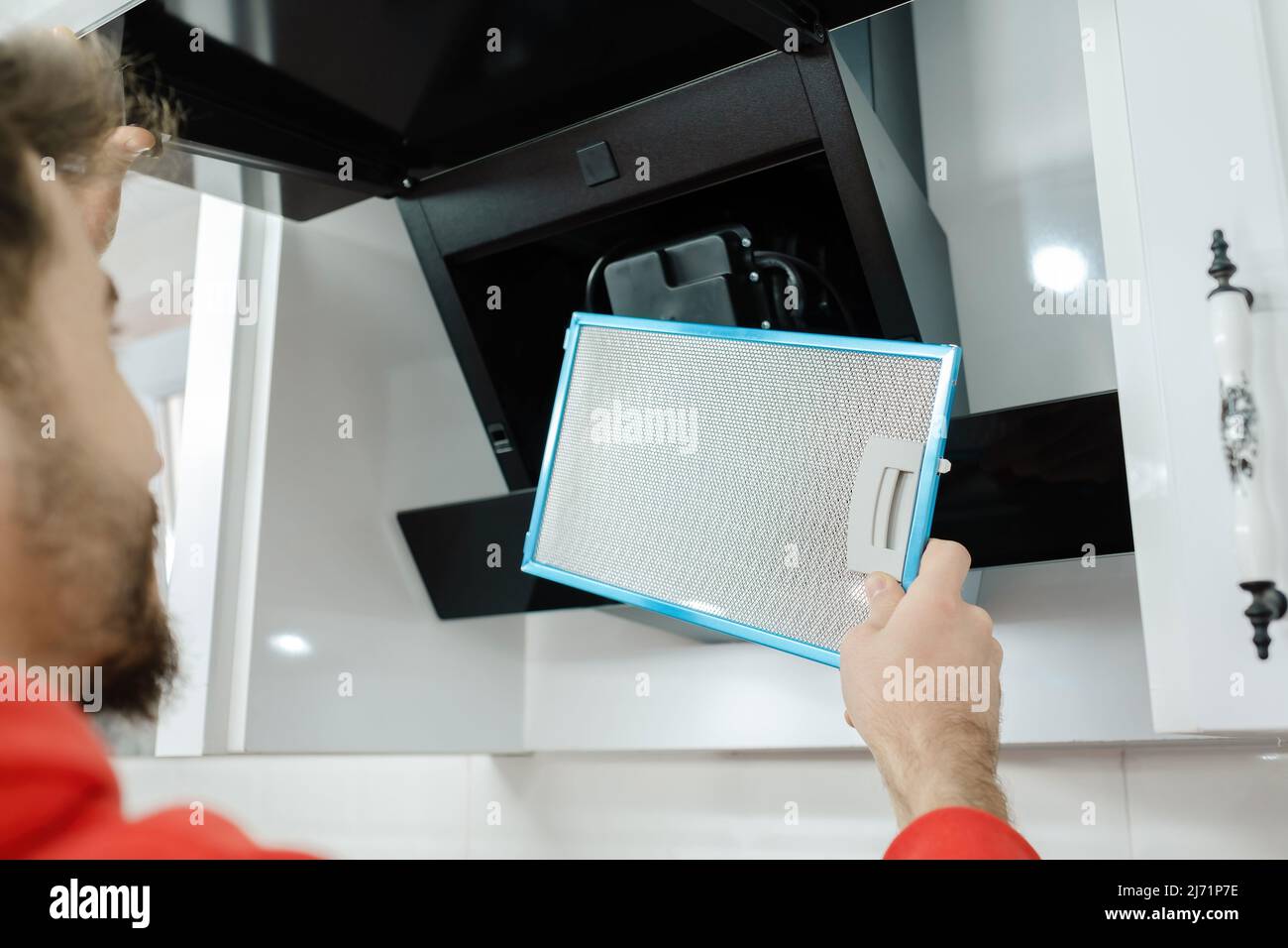 Mans hands removing a filter from cooker hood for cleaning or service. Replacing filter in kitchen hood. Modern kitchen fan or range hood. Stock Photo