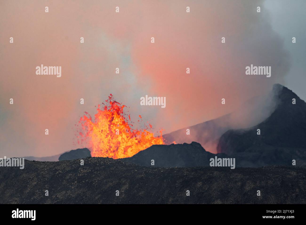 Rauchender aktiver Vulkankrater, Gluehende Lava spritzt ueber den Kraterrand, Vulkanausbruch, aktiver Tafelvulkan Fagradalsfjall Stock Photo