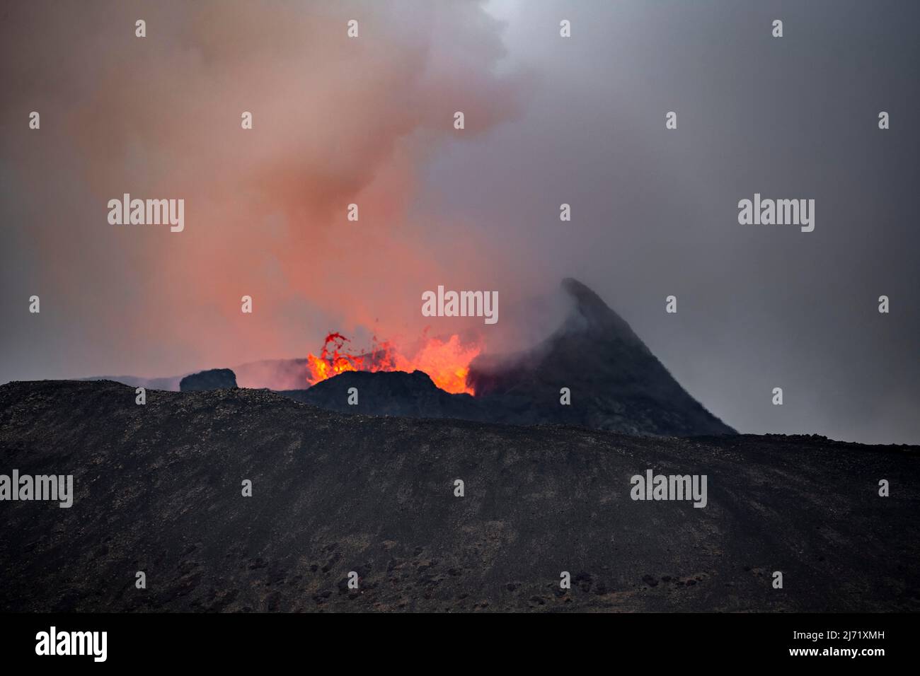 Rauchender aktiver Vulkankrater, Gluehende Lava spritzt ueber den Kraterrand, Vulkanausbruch, aktiver Tafelvulkan Fagradalsfjall Stock Photo