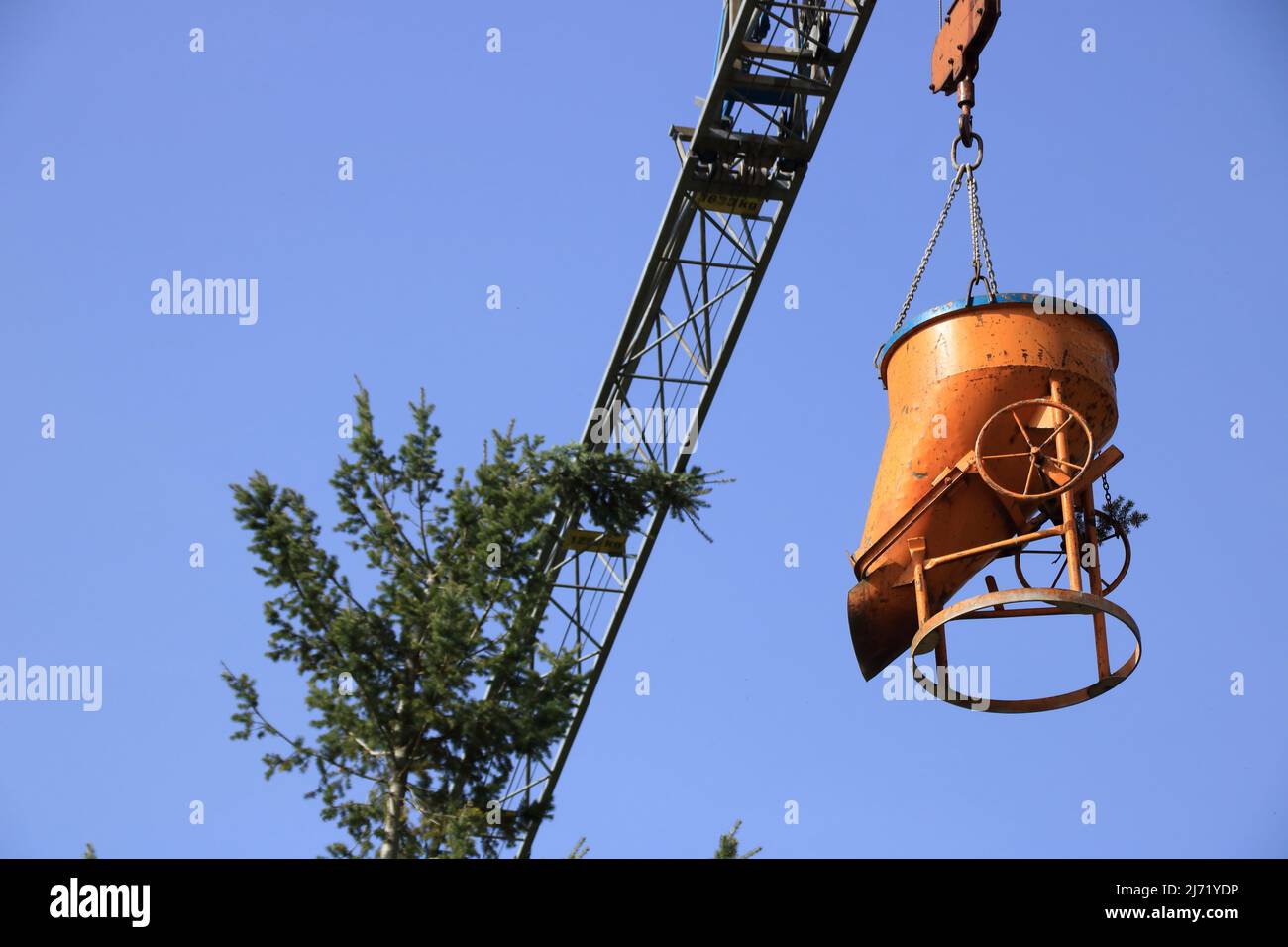 The boom of a construction crane snaps the top of a tree Stock Photo