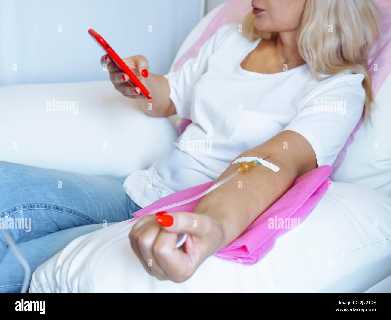 Woman Donor looking at mobile phone while needle is in arm , Closeup of arm with needle inserted into arm Stock Photo