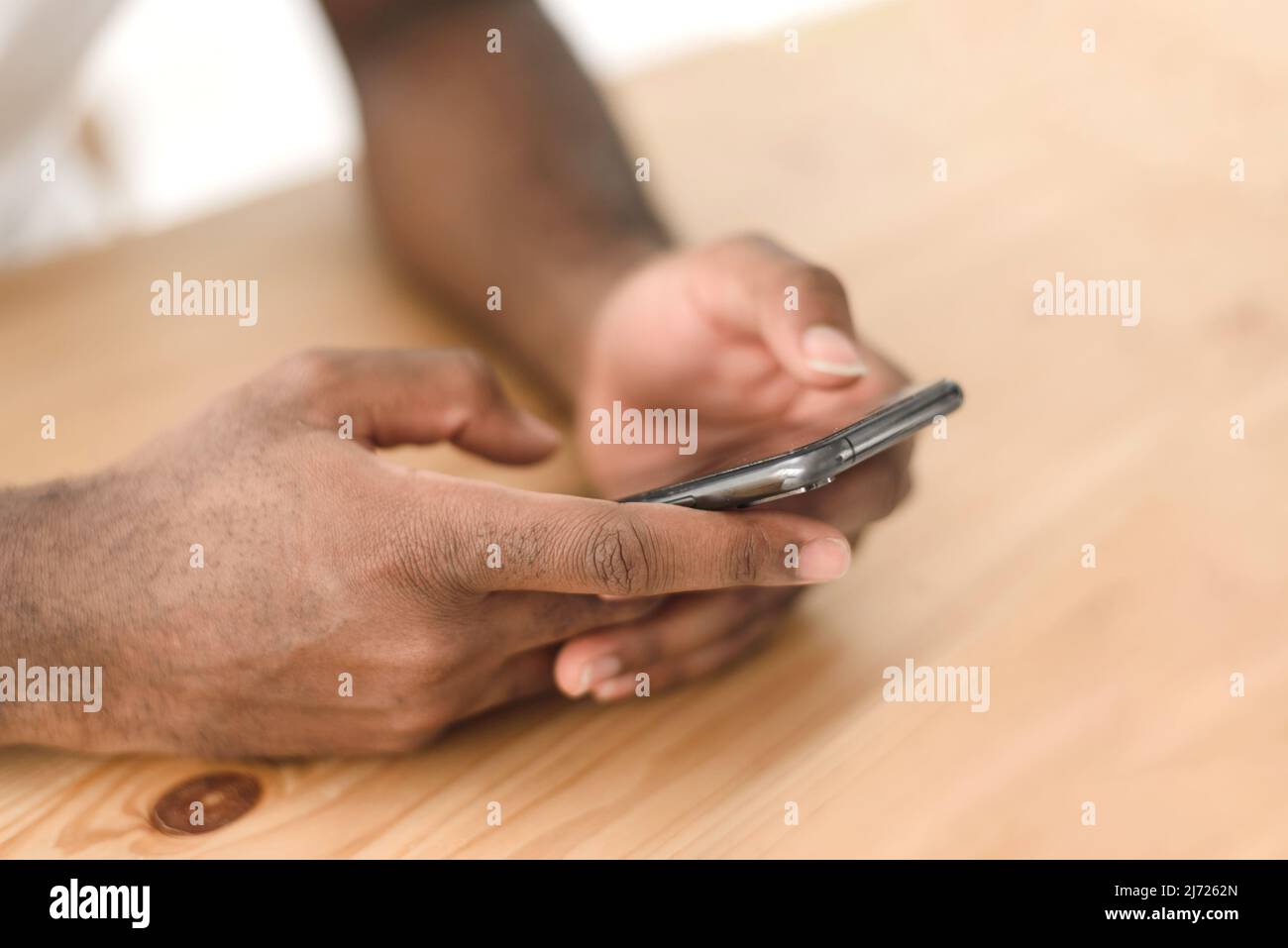Hands of a black man browsing social networks or reading news on the phone at the table Stock Photo