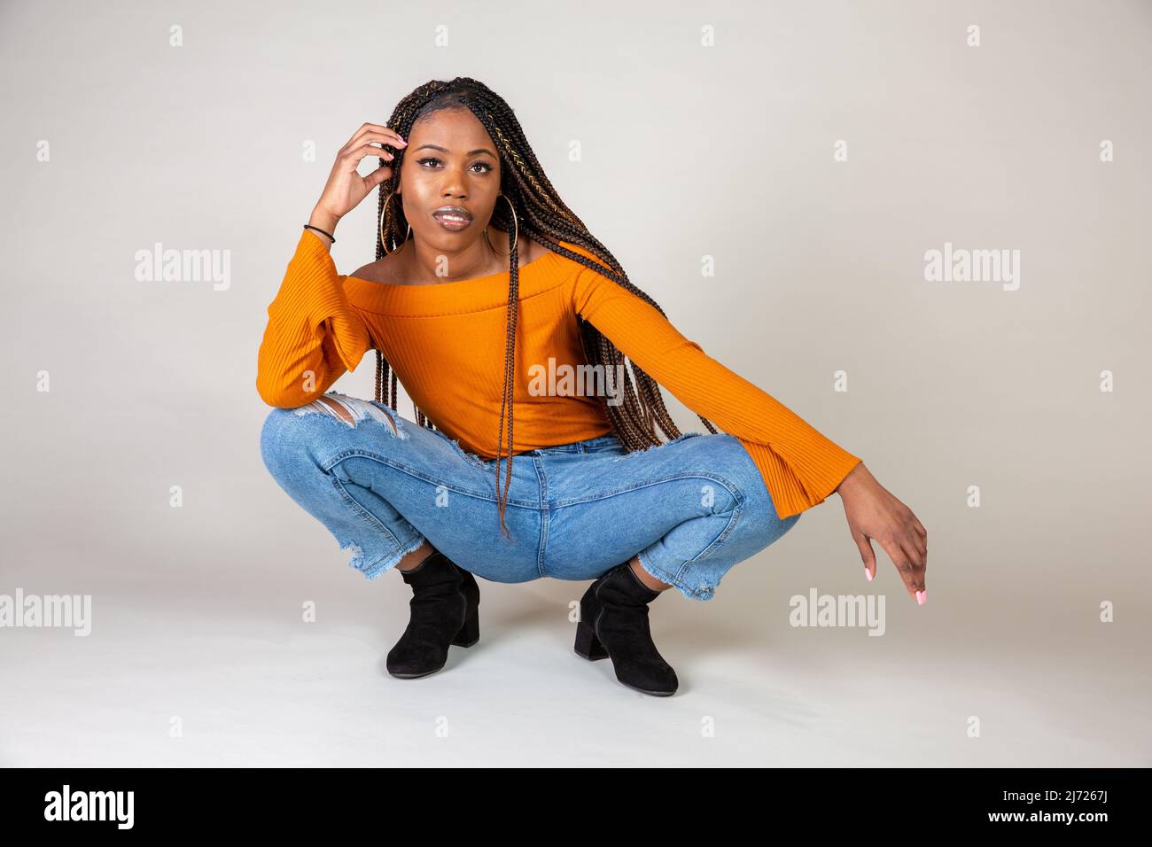 Studio shot of a young Black woman with vintage orange top and baggy jeans  posing on a white background squatting Stock Photo - Alamy