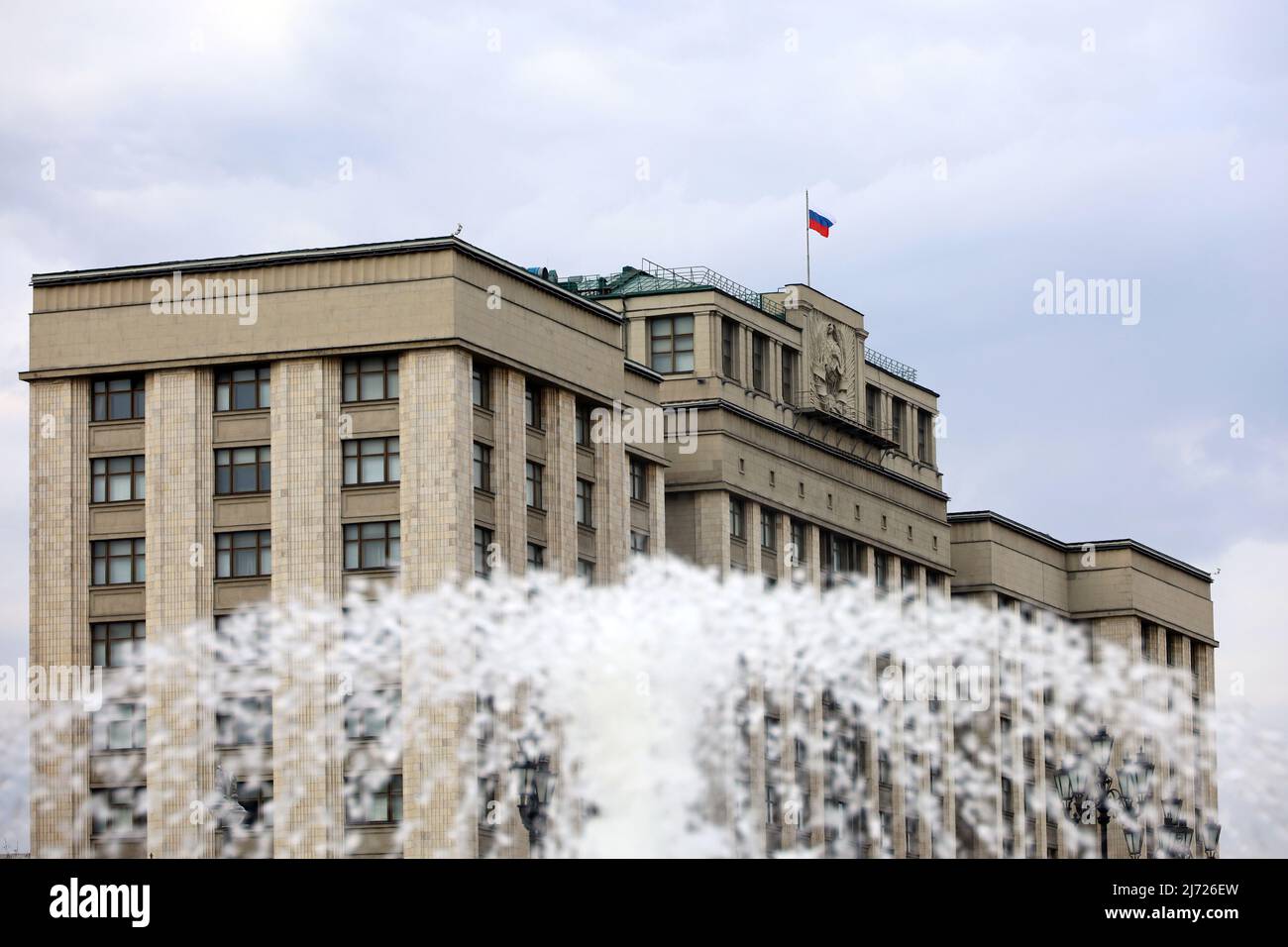 Russian flag on the parliament building in Moscow, view through the fountain splashes. Facade of State Duma of Russia, russian authority Stock Photo