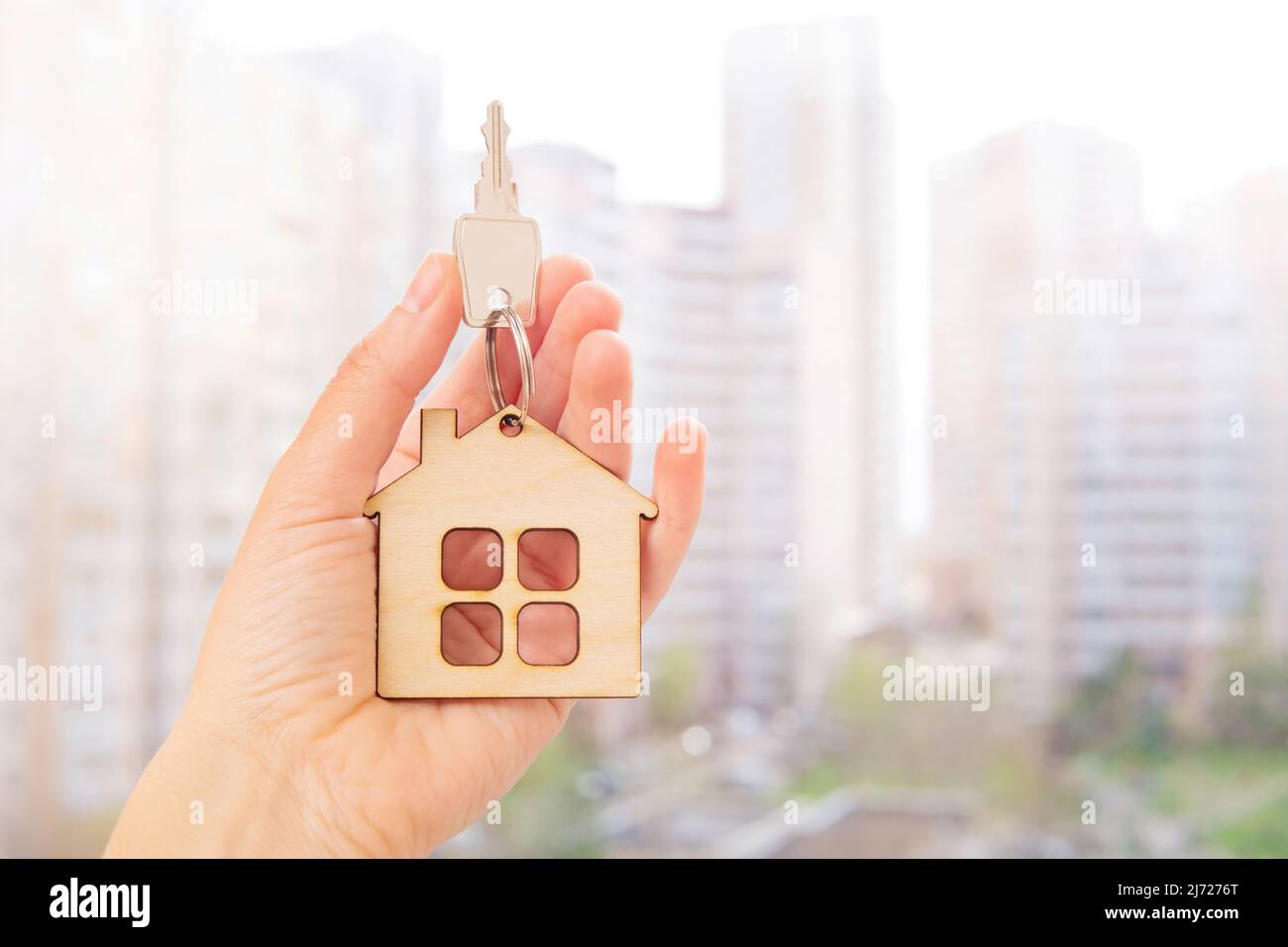 Key with a house shaped keychain in hand against a blurred city ...