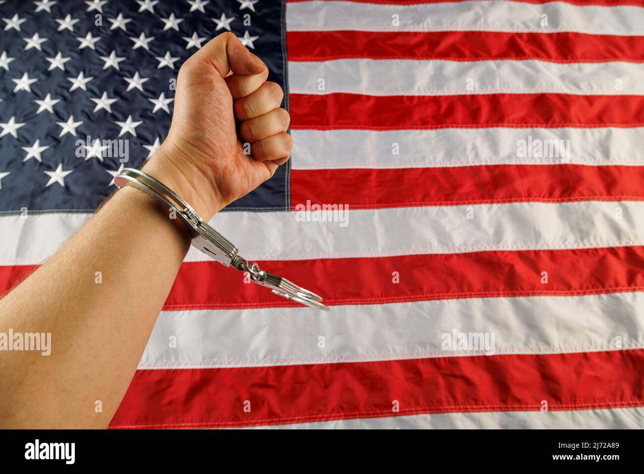 caucasian hand cuffed with silver metal handcuffs over US flag background Stock Photo