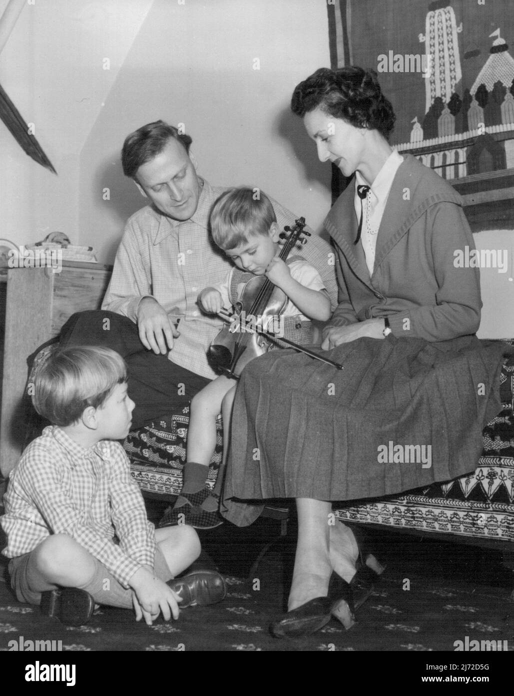 Another Genius In The Family -- The Menuhin family at their London home... Yehudi watches his youngest son try out a small violin.... Maybe there will be three genius's in the family soon. The celebrated violinist, Yehudi Menuhin is now in London for recitals of beethoven's sonatas.... In fact he's been in London some time, but the public meet him only at the concerts.... He does not seek publicity in other ways... Thirty eight year-old Menuhin was born in New York. His Parents are of Russian origin who went to America from pelestine... He was given his first violin at the age of four... When Stock Photo