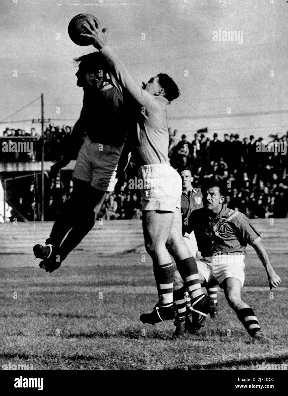 Ron Lord leaps into the air to talk the ball and save a desperate situation. NSW Goalkeeper Ron Lord, in brilliant form for NSW against the Australian Soccer team at the Sports Ground yesterday, flies in the air to take the ball from the head of Gordon Nunn. Harry Robertson looks on, awaiting the outcome of play. September 5, 1950. Stock Photo