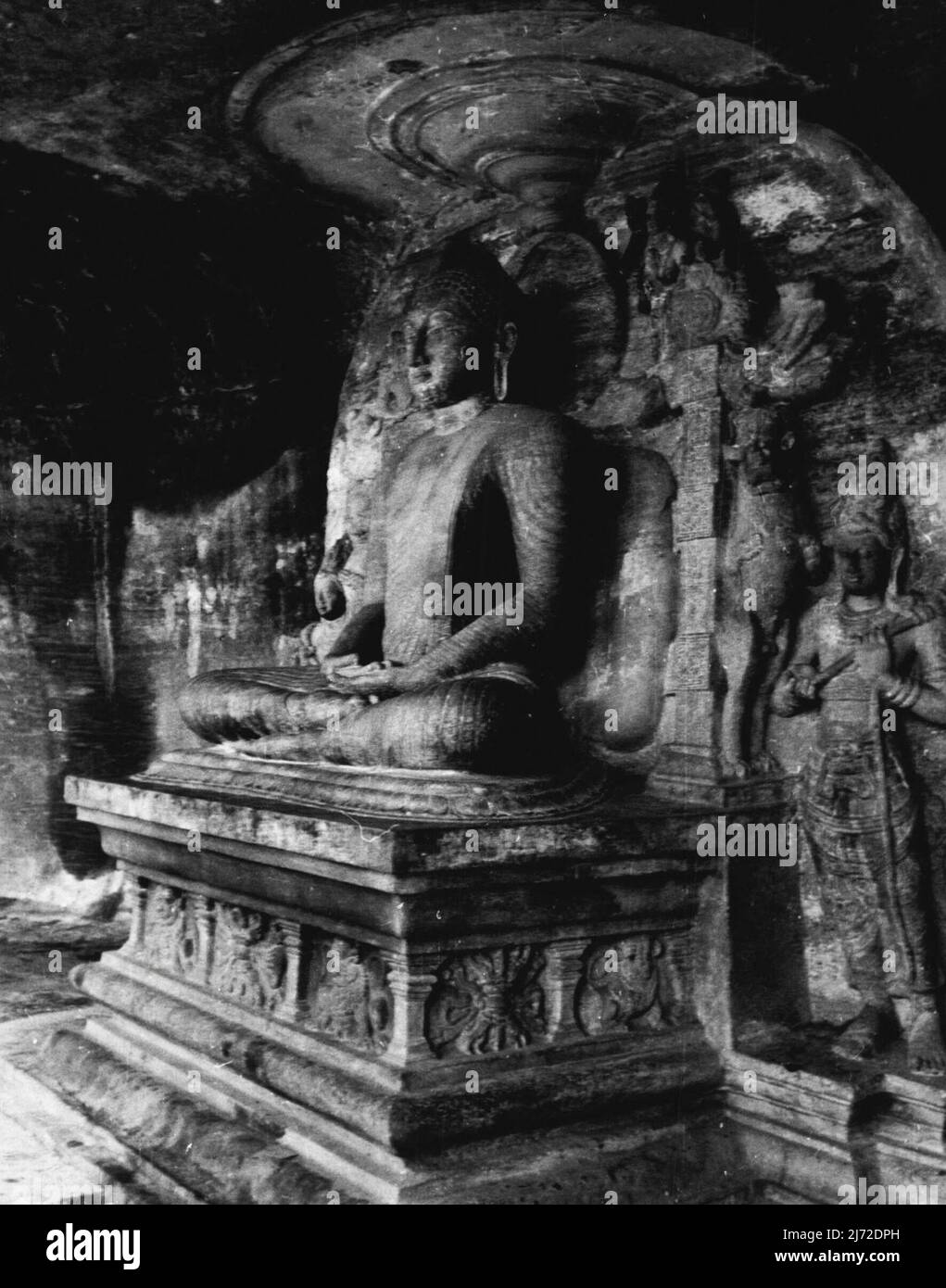 The Buried Cities' Of Ceylon - The rock-temple (Gal-vihara), 'the cave of the spirits of knowledge' is hewn out of a solid granite face, and in it broods a Buddha seated on a carved pedestal. The rock background is decorated with figures of Hindu gods, who played a considerable part in the religion of the Sinhalese Buddhists. July 18, 1942. (Photo by Paul Popper). Stock Photo