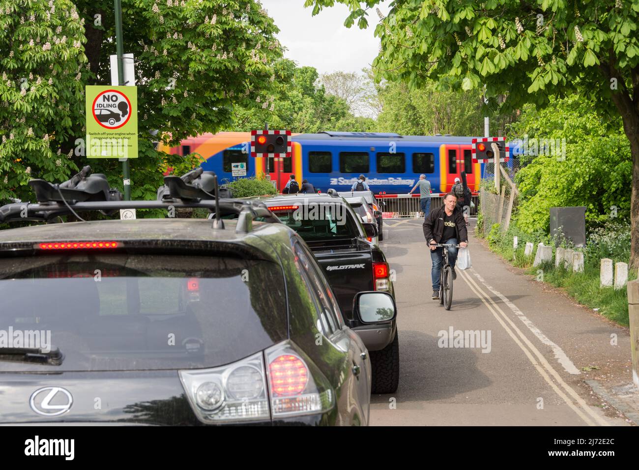 Stationary cars queuing and idling as a South Western Railway train passes Network Rail's Vine Road signal box in Barnes, London, SW13, England, UK Stock Photo