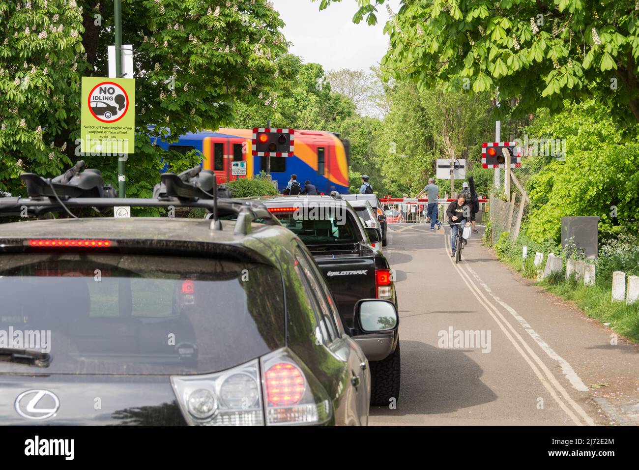 Stationary cars queuing and idling as a South Western Railway train passes Network Rail's Vine Road signal box in Barnes, London, SW13, England, UK Stock Photo