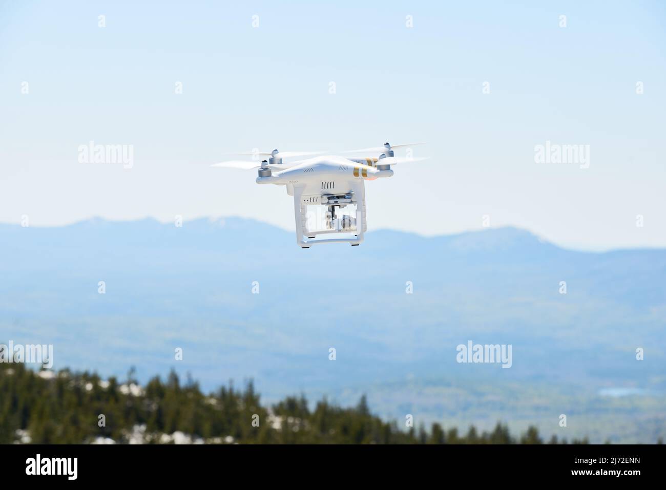 Making aerial shots with quadrocopter. Drone with camera flying over mountains and woods on a sunny day Stock Photo