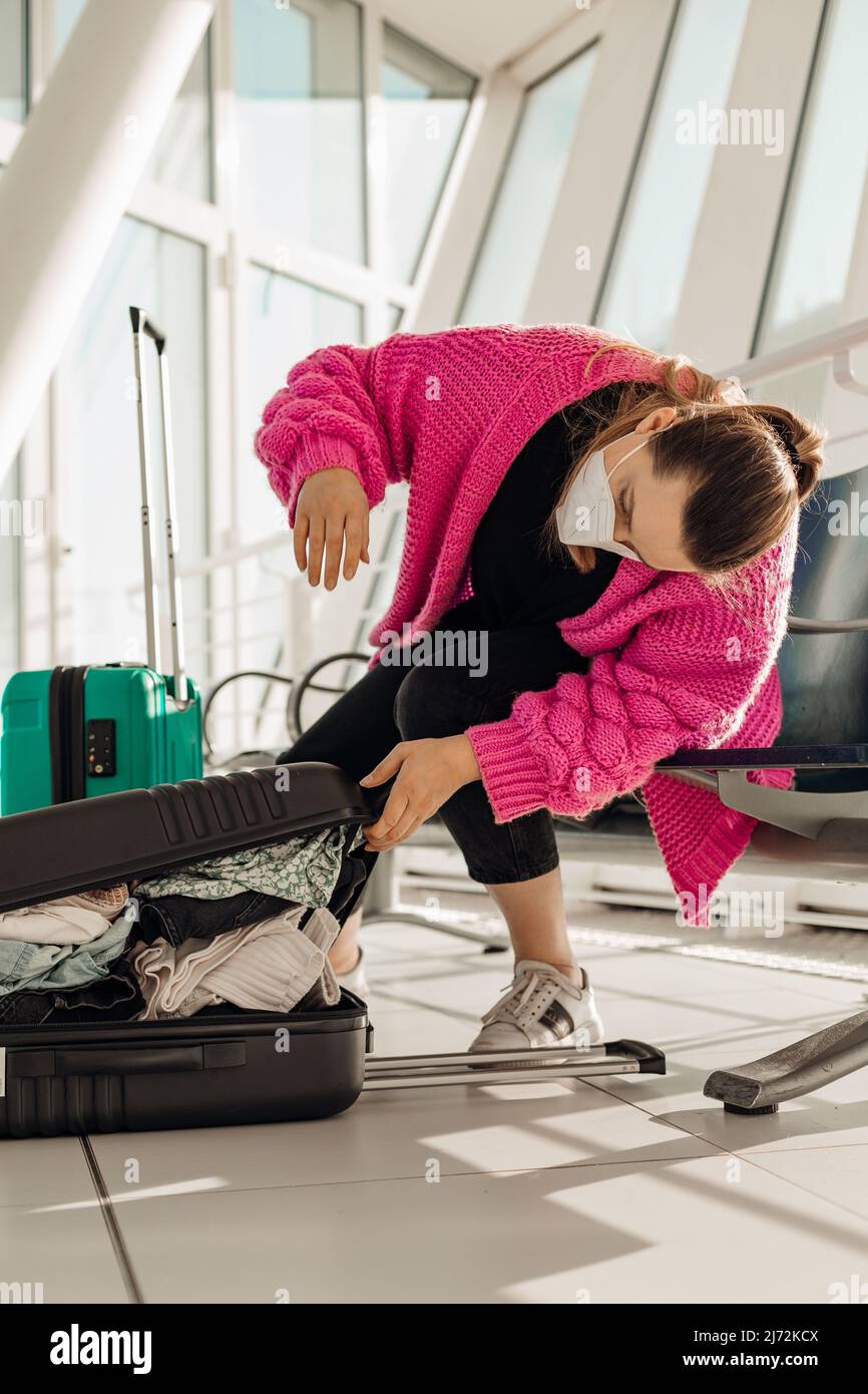 Vertical woman in pink jacket wearing face mask packing baggage sitting