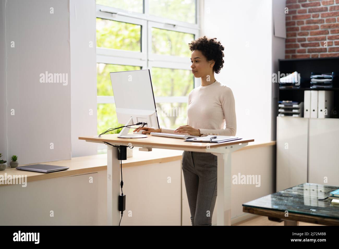 Woman Using Adjustable Height Standing Desk In Office For Good Posture