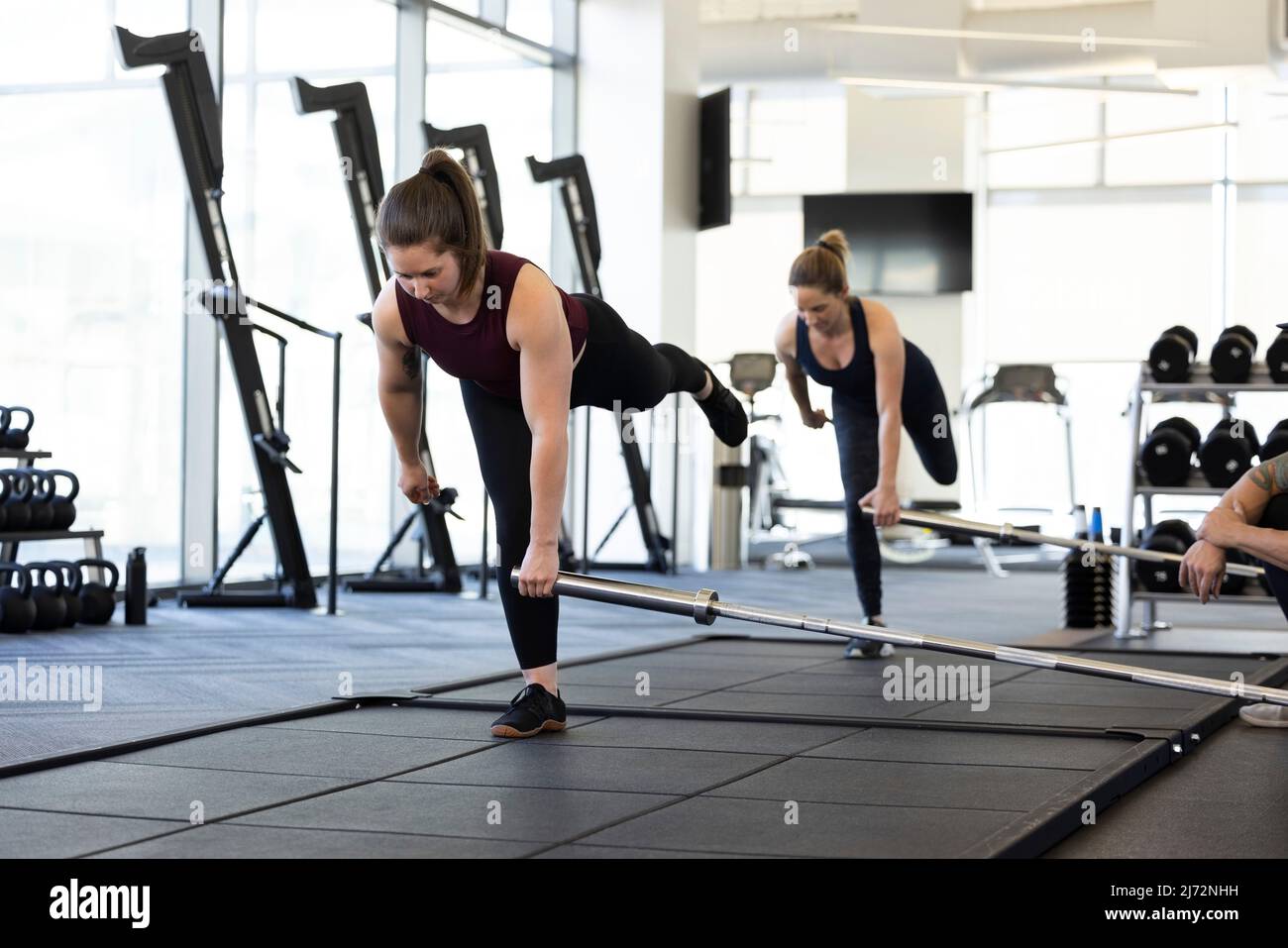 Two woman using a barbell, while standing on one foot during CrossFit