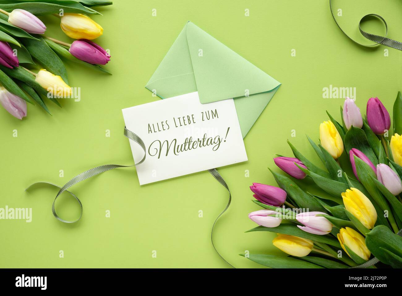 Alles Liebe zum Muttertag text, flat lay with colorful tulips, flat lay on paper with ribbons. Stock Photo