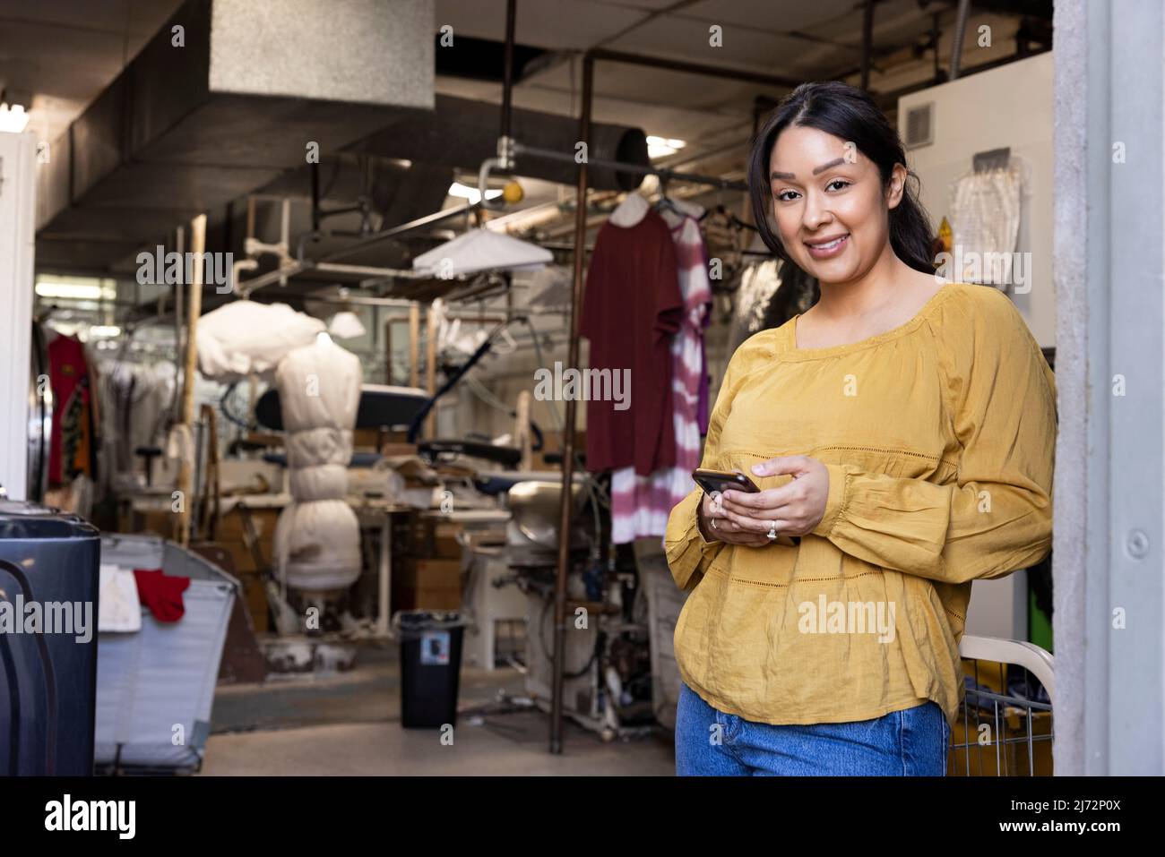 Portrait of a woman using her phone in back while working at dry cleaners. Stock Photo