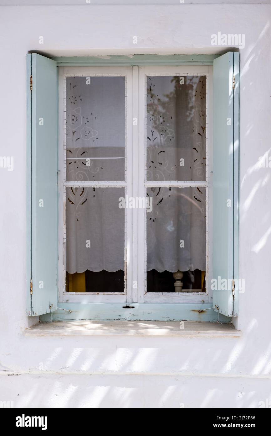 Window with pastel blue open wooden shutters on white wall. Cyclades ...