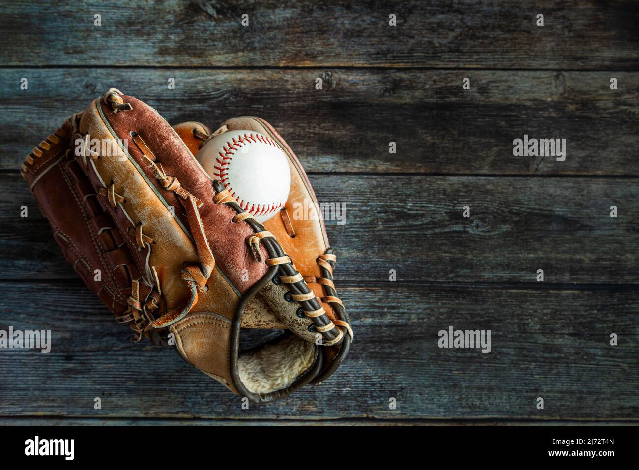 Leather baseball or softball glove with ball on rustic wooden background with copy space. Stock Photo