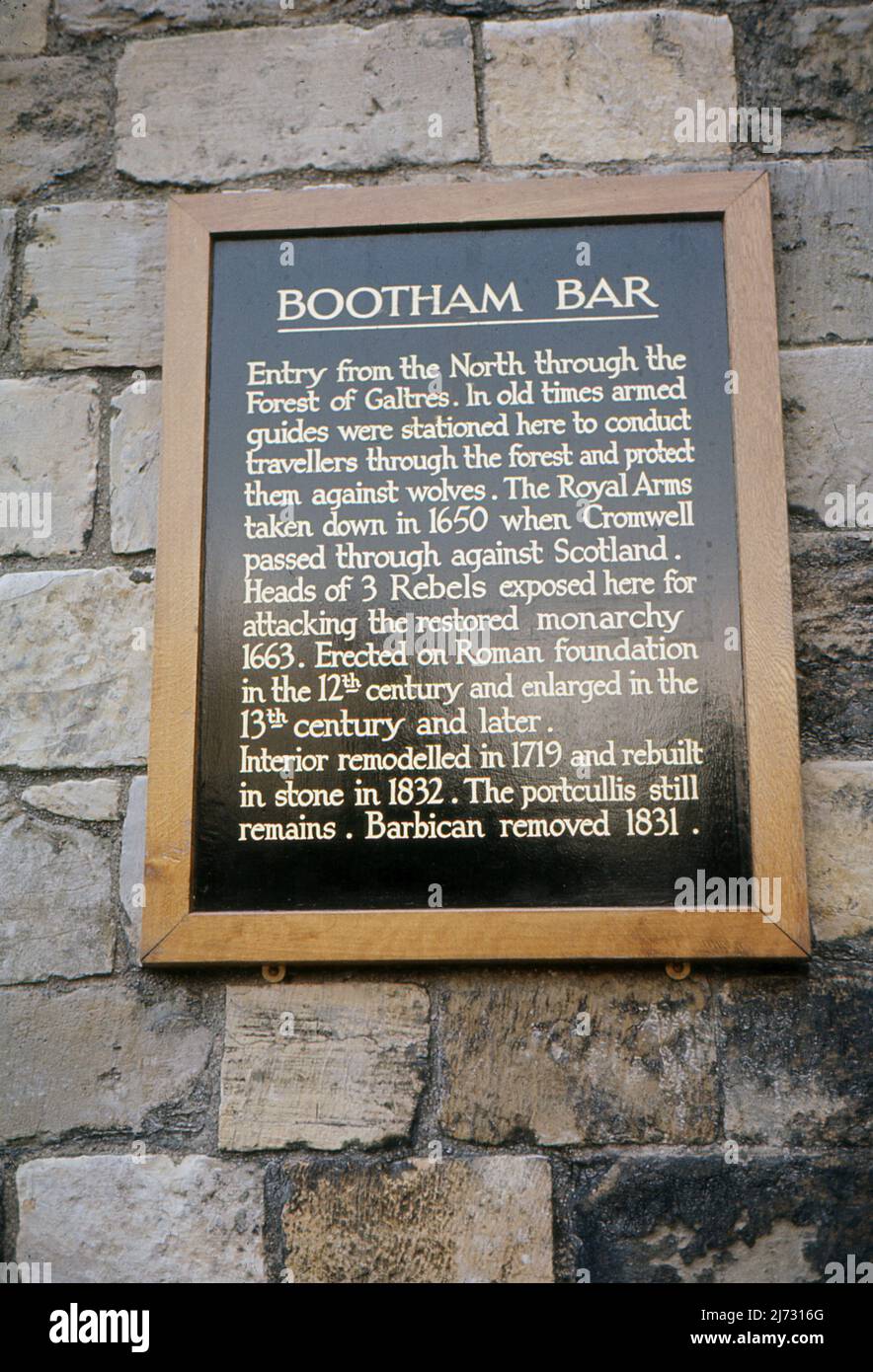 A sign attached to the wall of Bootham Bar, an imposing stone gateway way in York, North Yorkshire.  1967. The Sign provides the following history: “Bootham Bar: Entry from the North through the Forest of Galtres . In old times armed guides were stationed here to conduct travellers through the forest and protect them against wolves .The Royal Arms taken down in 1650 when Cromwell passed through against Scotland . Heads of 3 Rebels exposed here for attacking the restored monarchy 1663. Erected on Roman foundation in the 12th century and enlarged in the 13th century and later.......' Stock Photo