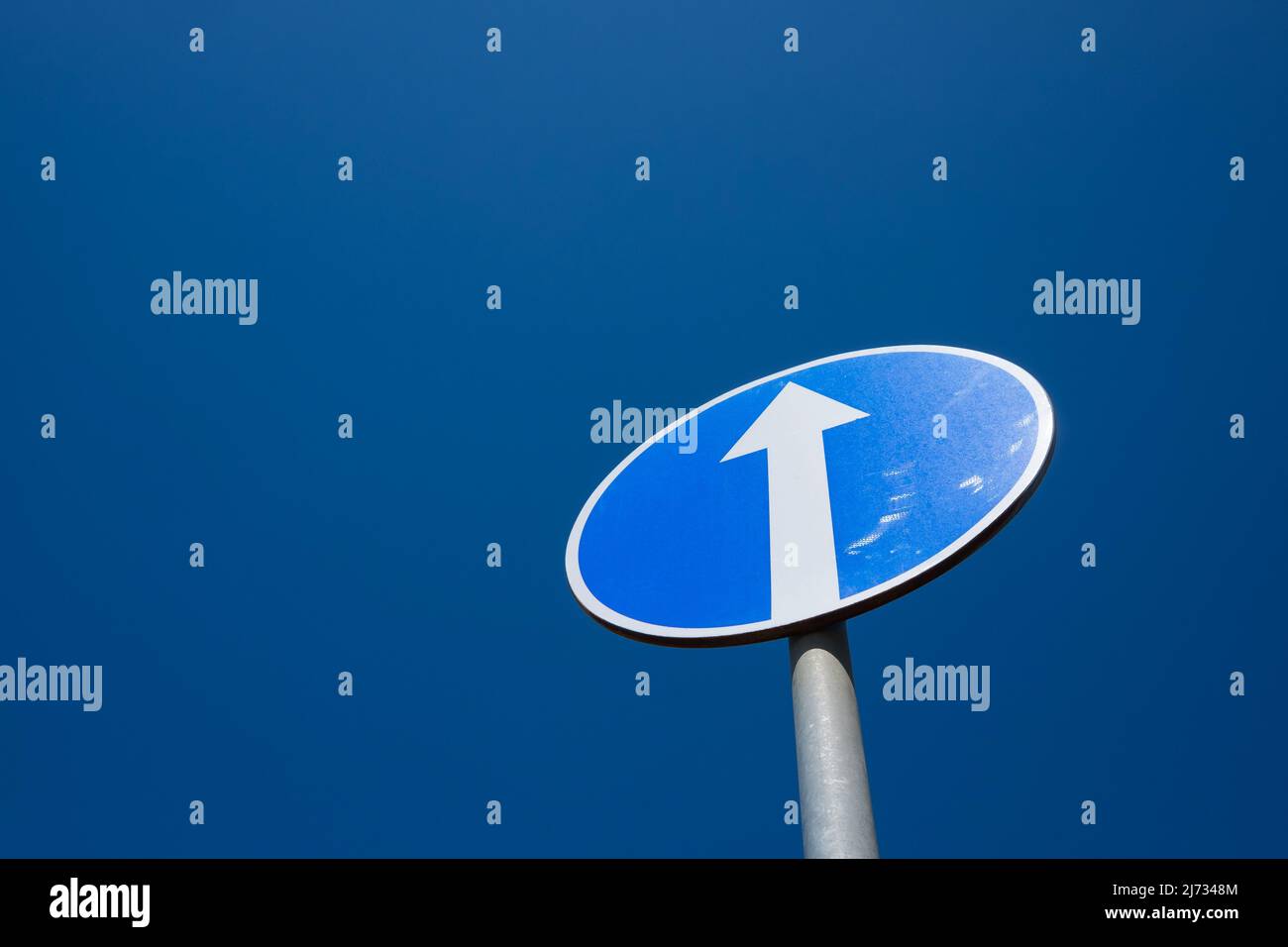 Circle road sign with white arrow on blue sky background. This sign