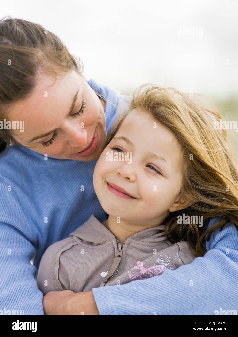 Mother wrapping her arms around young daughter at the beach Stock Photo
