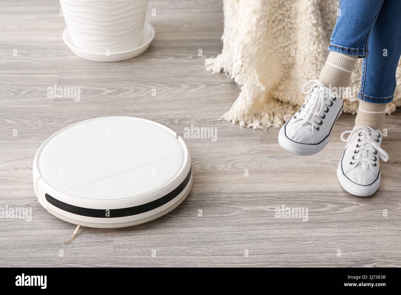 Modern robot vacuum cleaner near woman sitting on sofa at home Stock